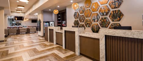 A hotel reception area with a herringbone patterned floor, a reception desk with a marble top, and hexagonal wall art.