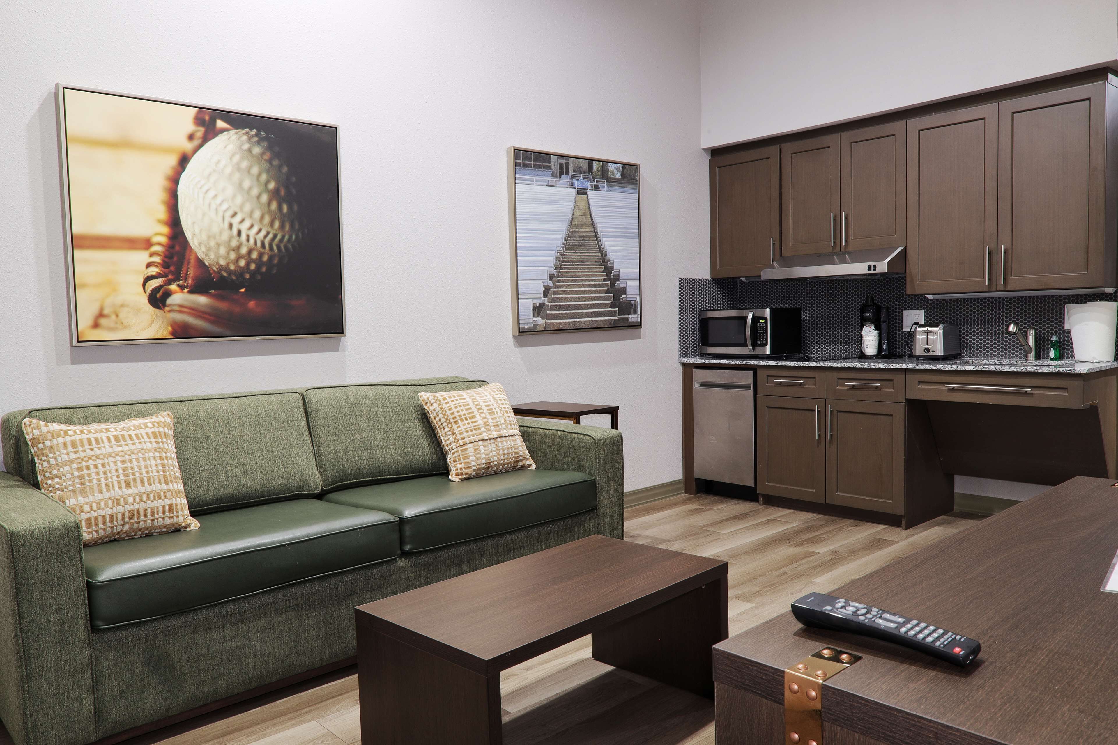 A modern living room with a green sofa, a coffee table, and a kitchen area with a microwave and cabinets.