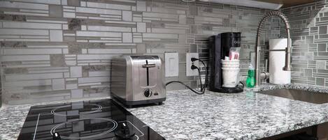 A kitchen with a granite countertop, a Kenyon induction cooktop, a toaster, a coffee maker, and a dishwasher.