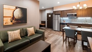 A modern kitchen with stainless steel appliances, a dining area with a table and chairs, and a living area with a sofa and cushions. - Hotel Manhattan, BW Signature Collection (New Caney)