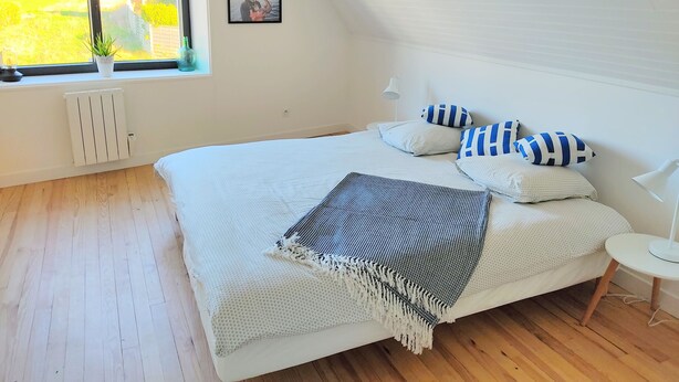 Un dormitorio con una cama grande, una ventana con vistas a la vegetación, un radiador y un cuadro en la pared.