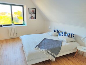 Een slaapkamer met een groot bed, een raam met uitzicht op groen, een radiator en een ingelijst kunstwerk aan de muur.