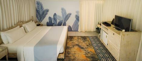 Un dormitorio con cama, televisor, cómoda y una pared con un mural de hojas.