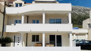 A two-story building with a balcony, a covered outdoor seating area, and a mountain backdrop. - Apartment Moon River (Dubrovnik)