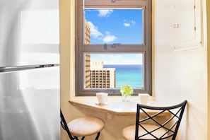 Una cocina con ventana a vista del océano, un refrigerador y dos sillas.