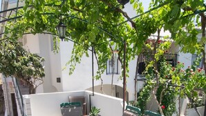 Une table à plateau en verre, entourée de chaises, de verdure et offrant une vue sur la rue.