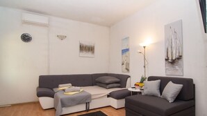 Un salon moderne avec un canapé gris, une petite table d’appoint sur laquelle se trouve une lampe, et des œuvres d’art accrochées aux murs.