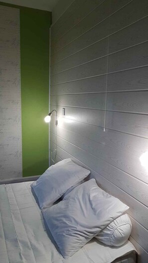 A room with a bed, two pillows, a green wall, and a light fixture above the bed.