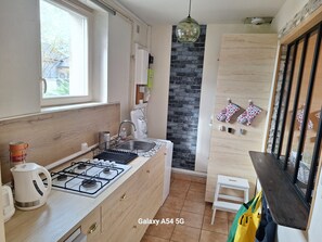 A modern kitchen with a gas stove, sink, and a window. There is a small table and a chair in the corner.