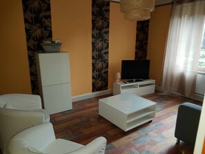 A living room with a sofa, a coffee table, a TV on a stand, a cabinet, and patterned wallpaper.