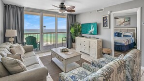 Uma sala de estar com sofá, mesa de centro e televisão. Há uma varanda com vista para o oceano.
