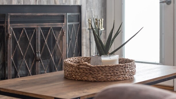 Ein Wohnzimmer mit einem flachbildfernseher über einem Kamin, einem Korbwicker-Korb mit Kerze und Pflanze auf einem Holztisch und einer Tür mit Milchglasfenster.
