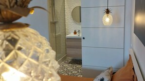 A bedroom with a bed, a hanging light fixture, and a view into a bathroom. - Le Bompard*** 50 m² Art Deco villa with garden (Rodez)