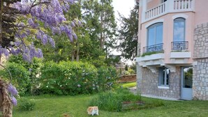 A house with a stone facade, a balcony with a metal railing, and a well-maintained garden with purple flowers and a cat. - Le Bompard*** 50 m² Art Deco villa with garden (Rodez)
