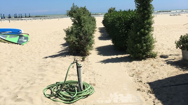 Una playa arenosa con cielo despejado, una manguera verde y un bote azul.
