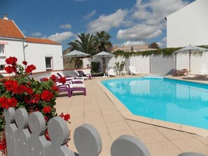 A swimming pool area with lounge chairs, umbrellas, and a white building in the background. - Location Classée 3*** - 4 rooms - 6 people - heated swimming pool (Sallertaine)