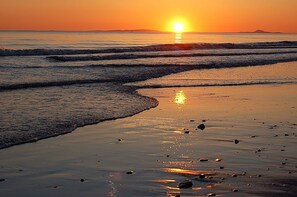 Une plage au coucher du soleil, où les vagues viennent doucement lécher le rivage.