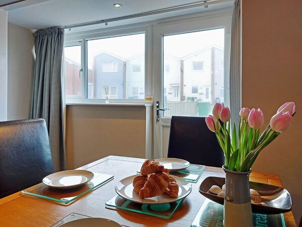 A dining table with croissants, a vase with tulips, and a view of residential buildings through a window.