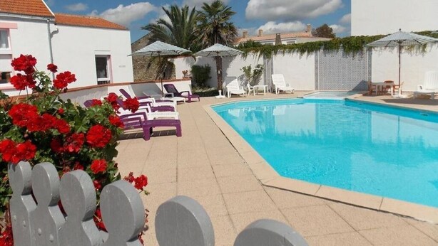 Area piscina con lettini, ombrelloni e un edificio bianco sullo sfondo.