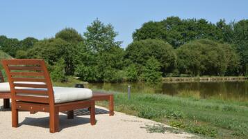 A wooden bench with a cushion by a lake, surrounded by trees and a clear sky.