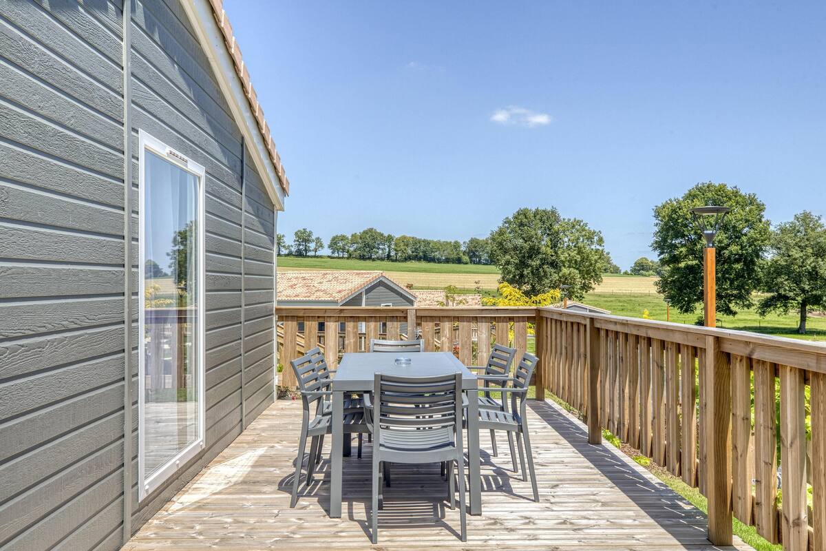 Une terrasse avec une table et des chaises, une balustrade en bois et une vue sur un paysage verdoyant.