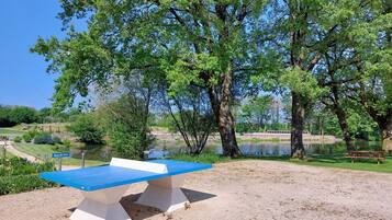 A picnic table with a blue top and white base, surrounded by trees and a lake.