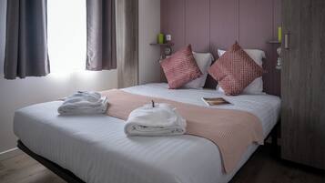 A neatly made bed with towels, a pink throw blanket, and two red patterned pillows.