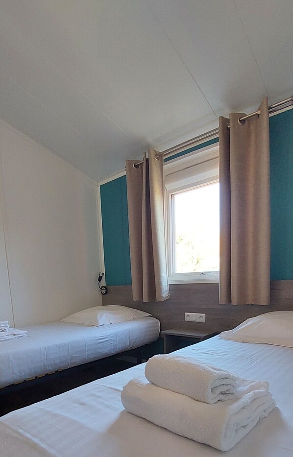 A hotel room with two single beds, a window with curtains, and a wall-mounted phone.