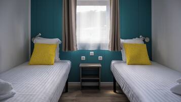 A twin room with two single beds, each with a white bedspread and a yellow pillow with white polka dots. There is a small wooden nightstand between the beds.