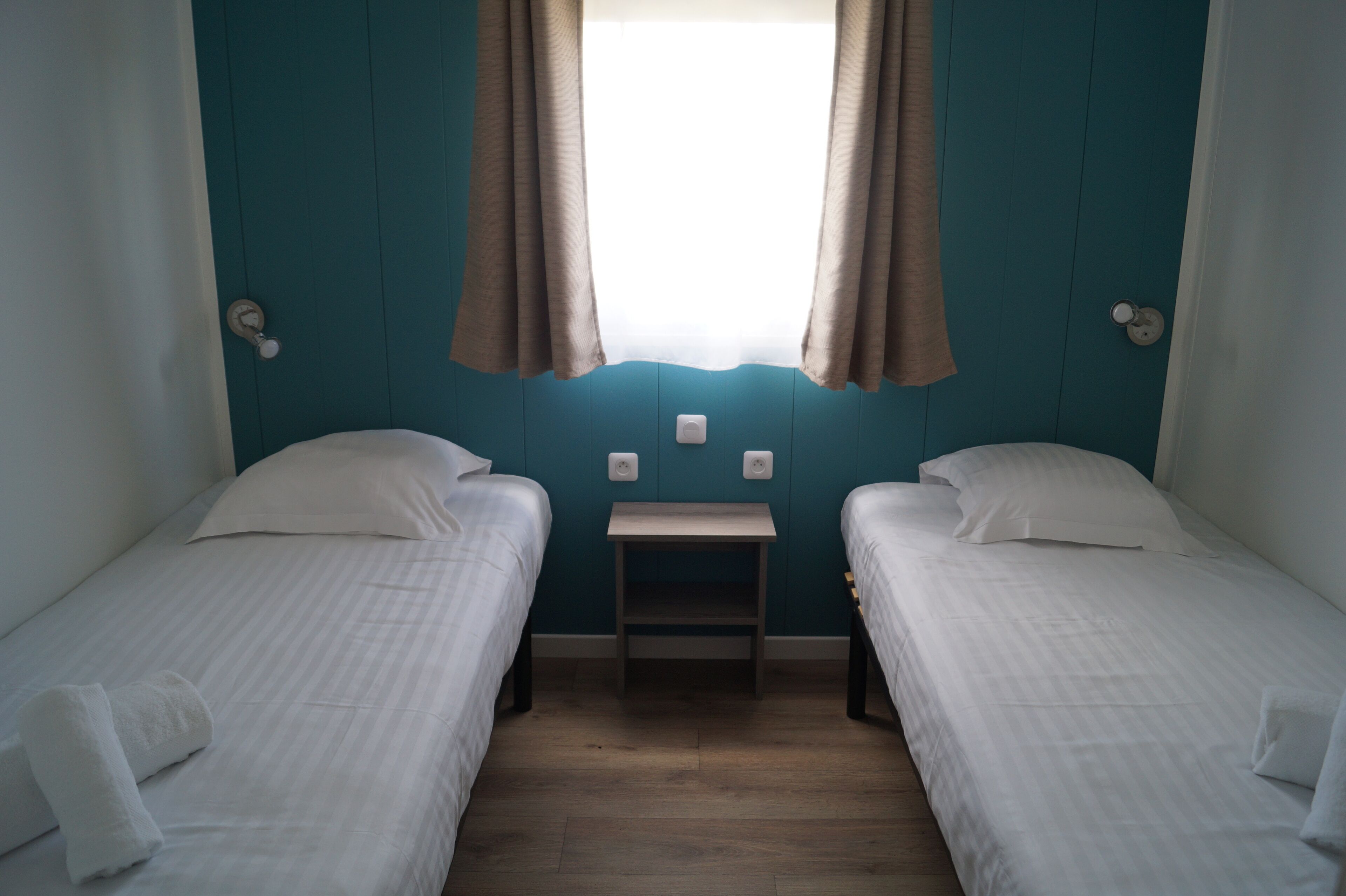 A room with two single beds, a small table, and a window with curtains.
