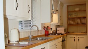 A kitchen with white cabinets, a wooden countertop, a sink, a stove, and a tiled floor.