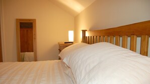 A bedroom with a wooden headboard, a bedside table with a lamp, and a door leading to another room.