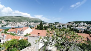 A coastal cityscape with terraced buildings, a prominent hill, and a clear blue sky. - Guest House Misita (Dubrovnik)