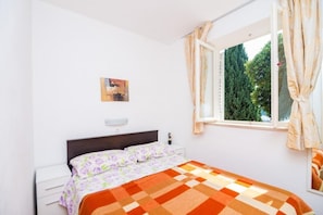 A bedroom with a bed, a nightstand, a window with curtains, and a wall-mounted picture.