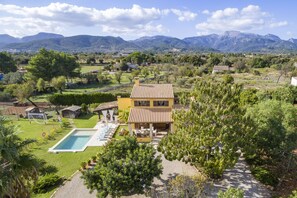 Una villa con piscina, rodeada de exuberante vegetación y montañas al fondo.
