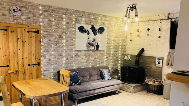 A cozy living room with a brick wall, a wooden door, a gray sofa, a wooden table, and a fireplace. - The Cuddly Cow Cosy Barn Studio Campview Farm Stay (Ballyshannon)