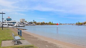 Un puerto deportivo con barcos amarrados, cielo despejado y un camino peatonal con bancos.