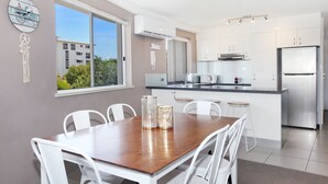 Una cocina moderna con armarios blancos, un refrigerador de acero inoxidable y un comedor con mesa de madera y sillas blancas.