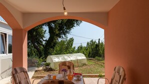 An outdoor patio with a table set for two, two chairs, a light bulb, and a greenhouse in the background. - Apartment Nike (Zupa dubrovacka)