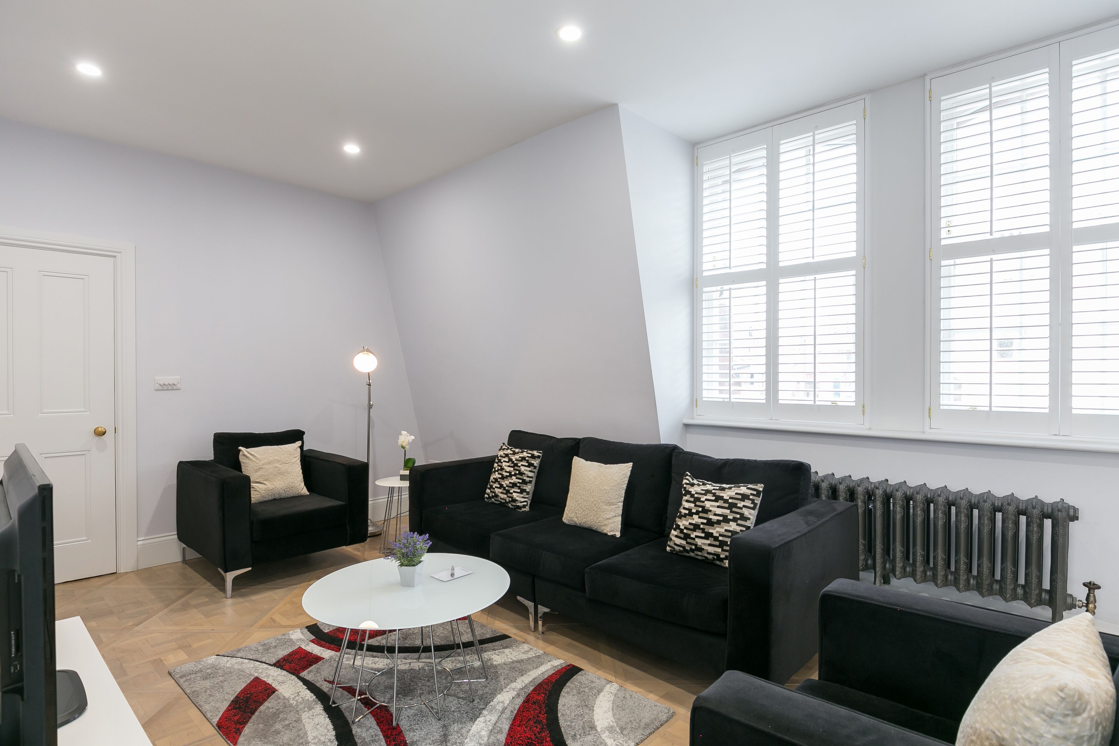 A modern living room with a black sofa, a white coffee table, and a red and gray rug.