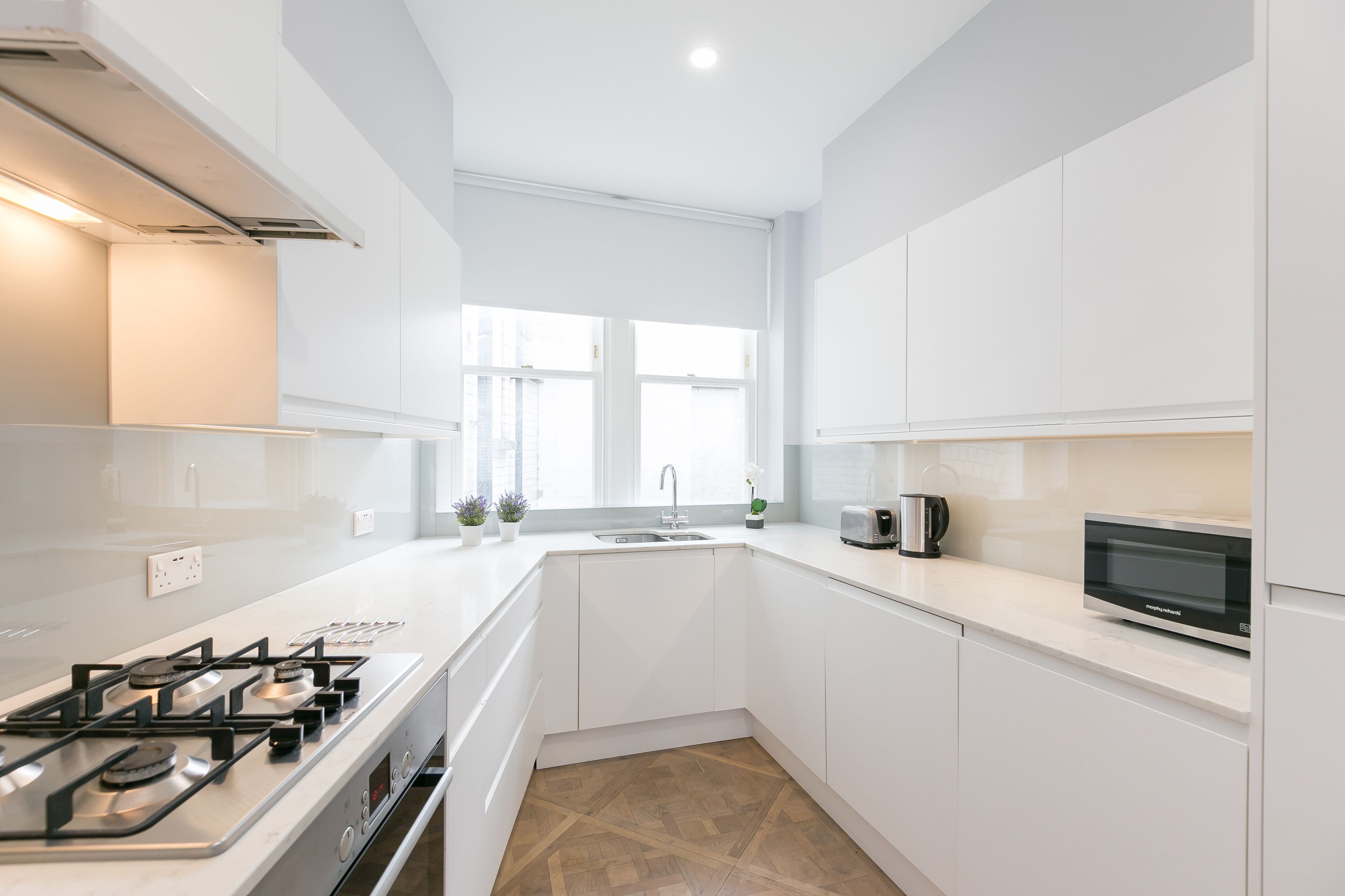 A modern kitchen with white cabinetry, a gas stove, a microwave, and a sink.