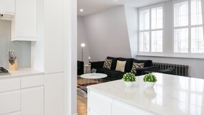 A modern kitchen with white cabinets, a marble countertop, and two potted plants.