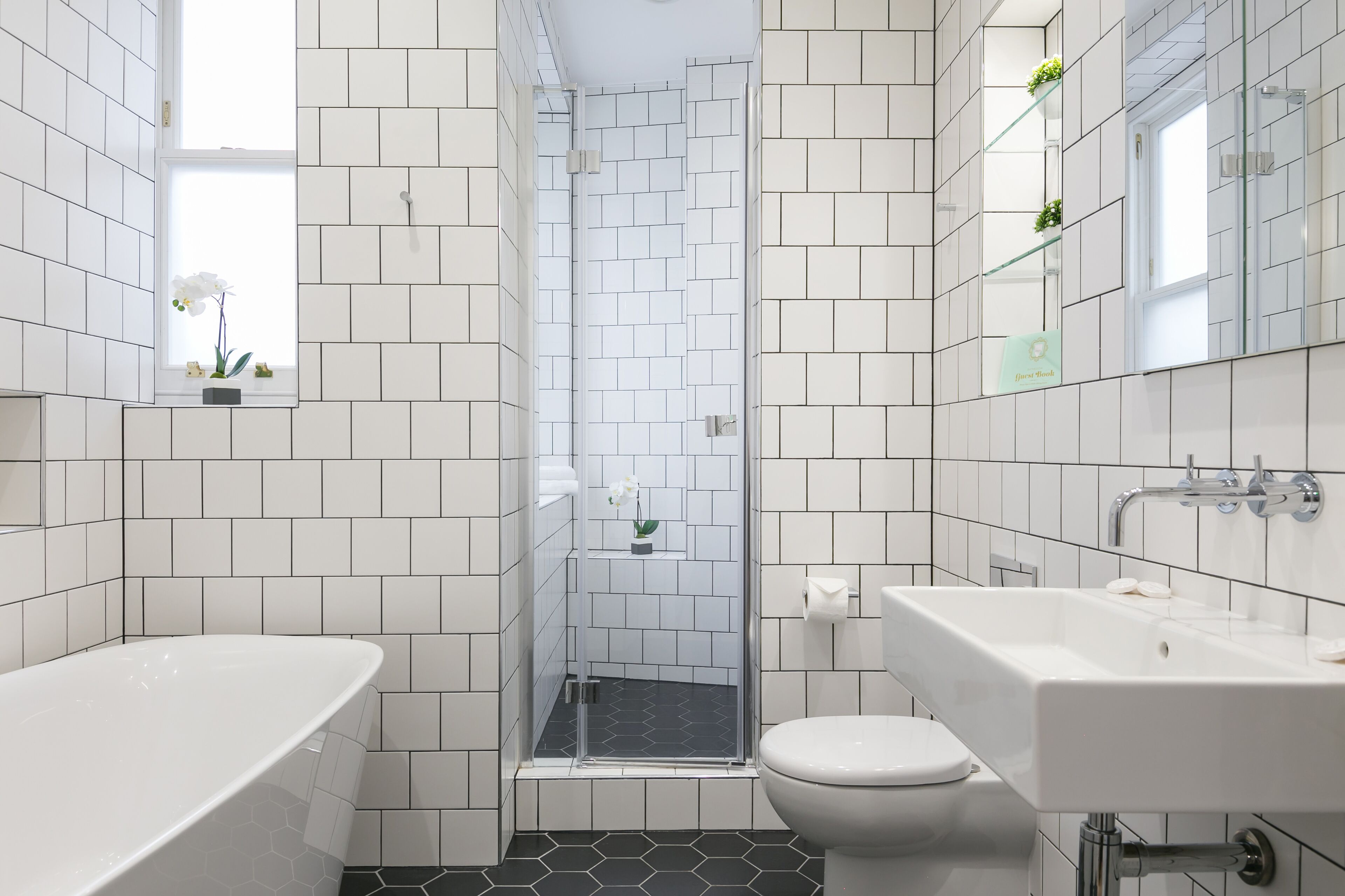 Un baño moderno con azulejos blancos, cabina de ducha de vidrio, bañera blanca y lavabo con espejo.