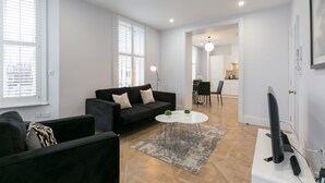 A modern living room with a black sofa, a white coffee table, and a flat-screen TV.