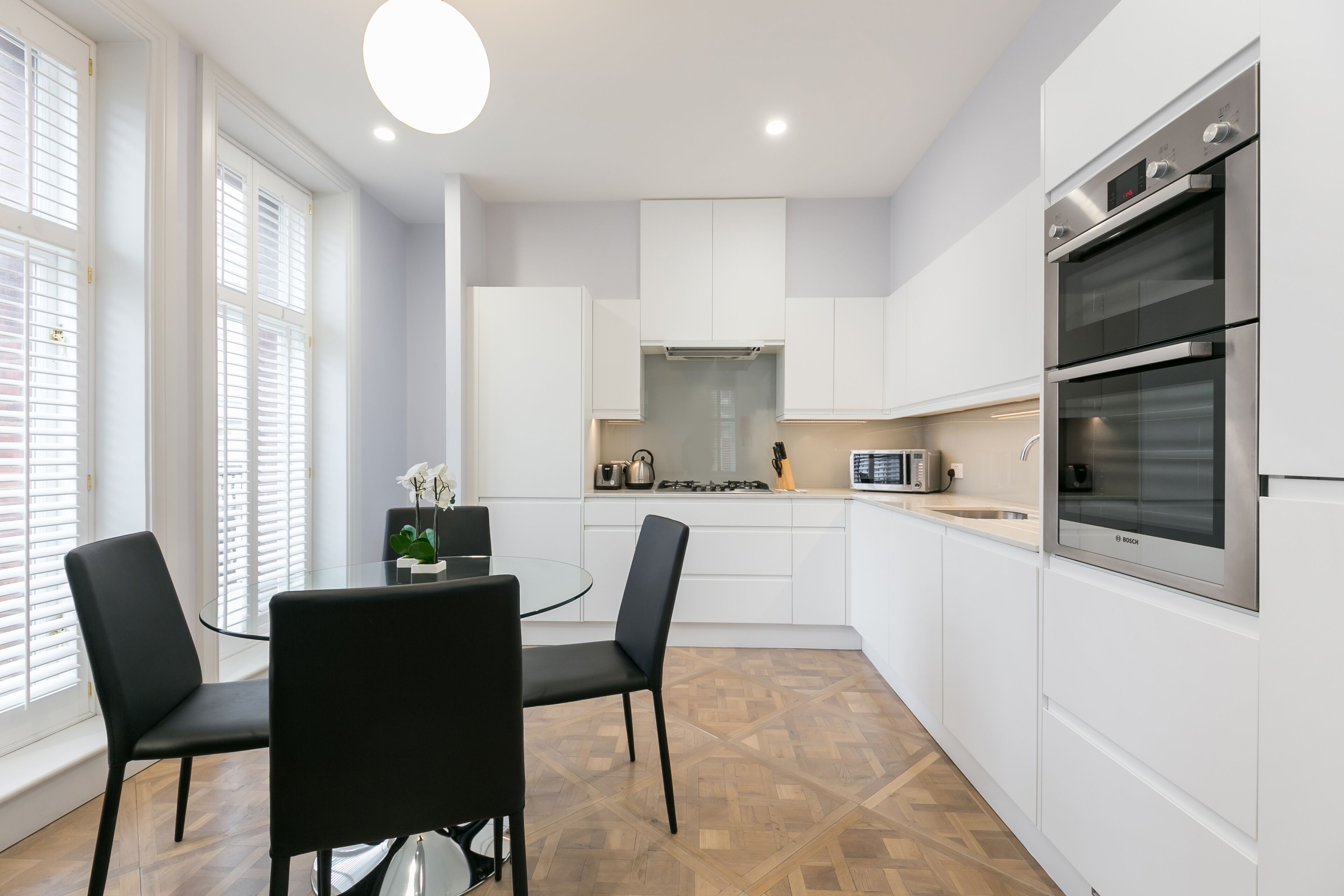 A modern kitchen with white cabinets, a Bosch oven, and a dining area with black chairs and a glass table.