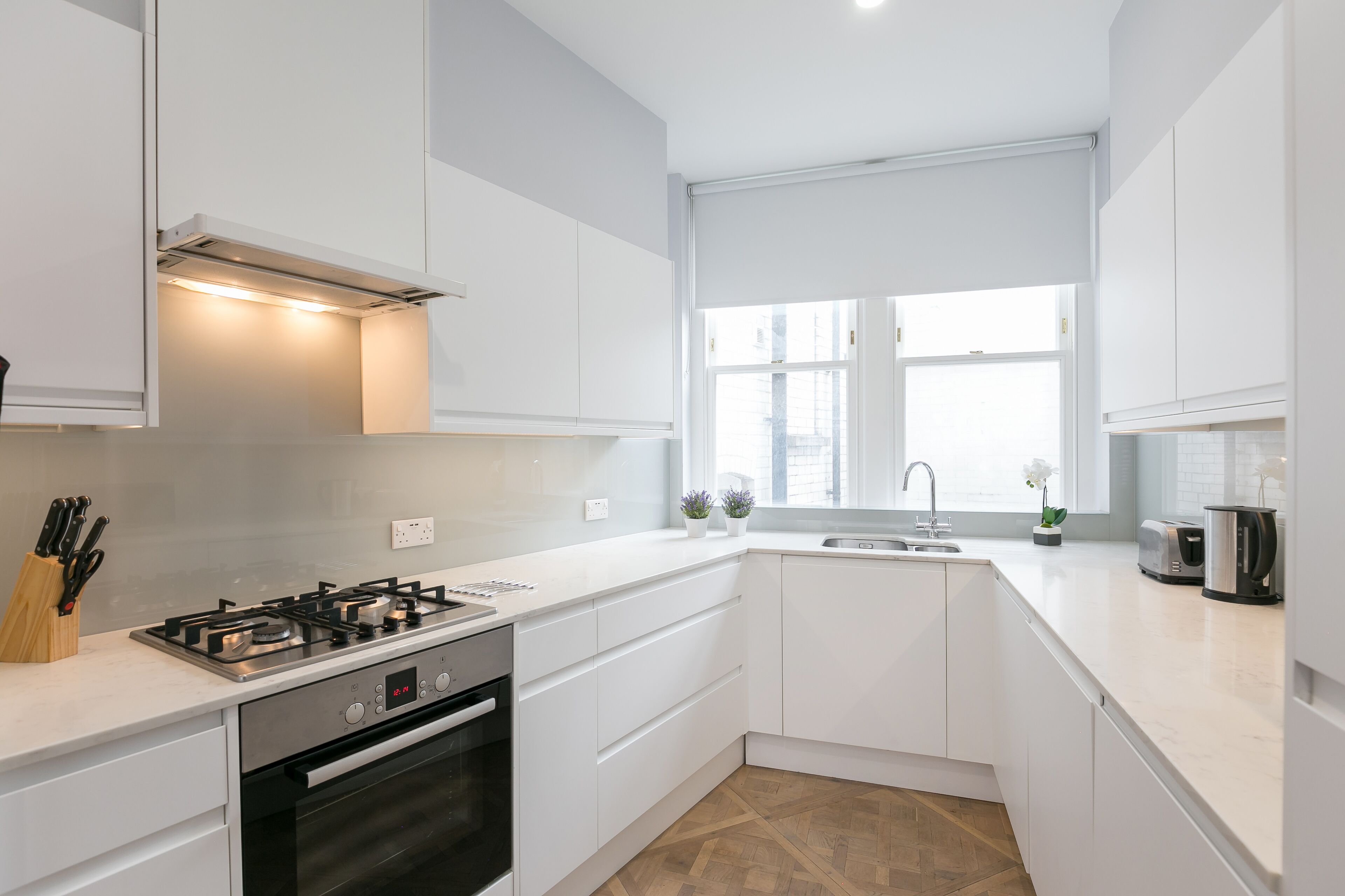A modern kitchen with white cabinetry, a built-in oven, a gas stove, and a window providing natural light.