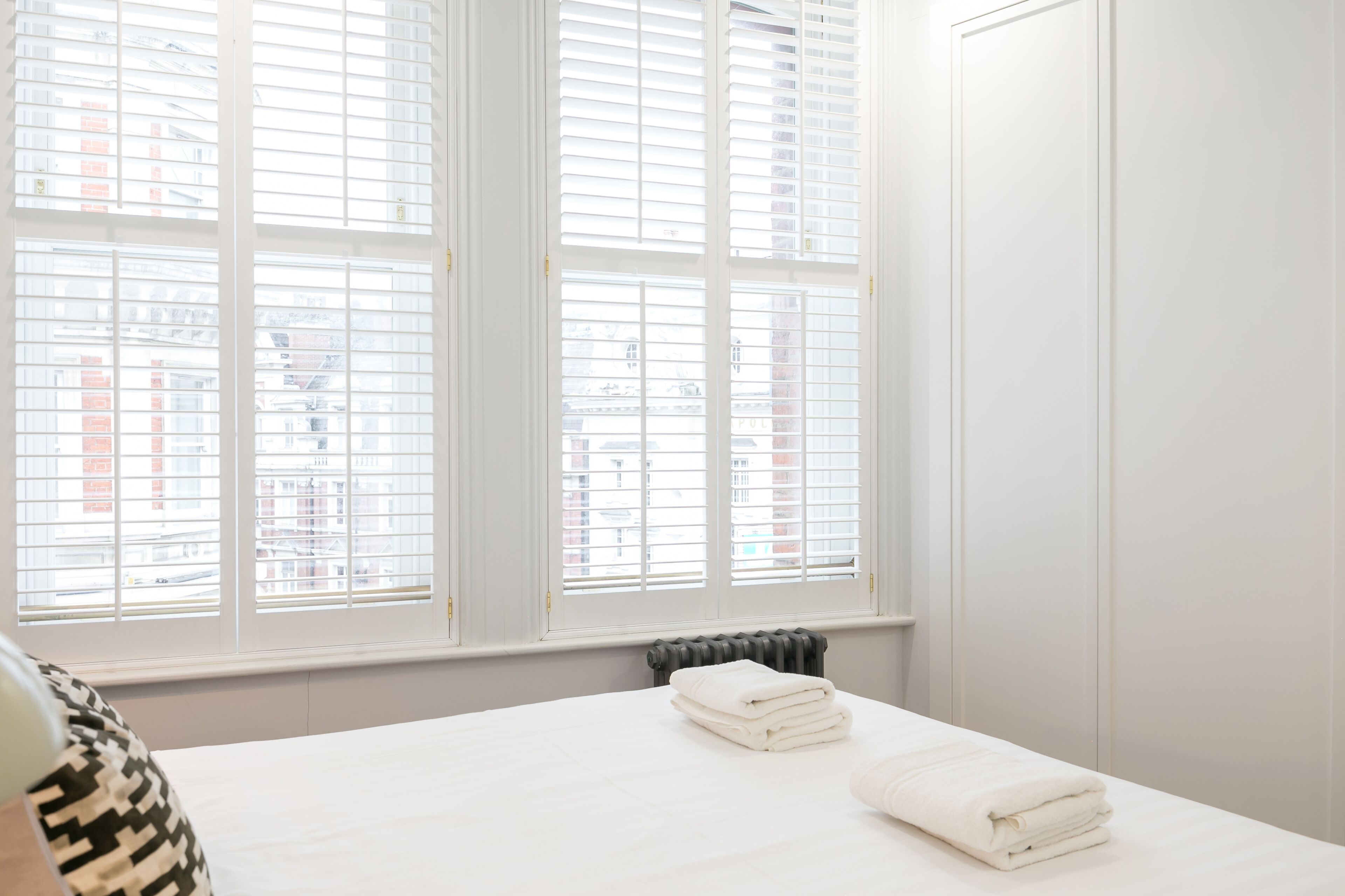 A hotel room with a bed, white curtains, and a view of buildings through the window.