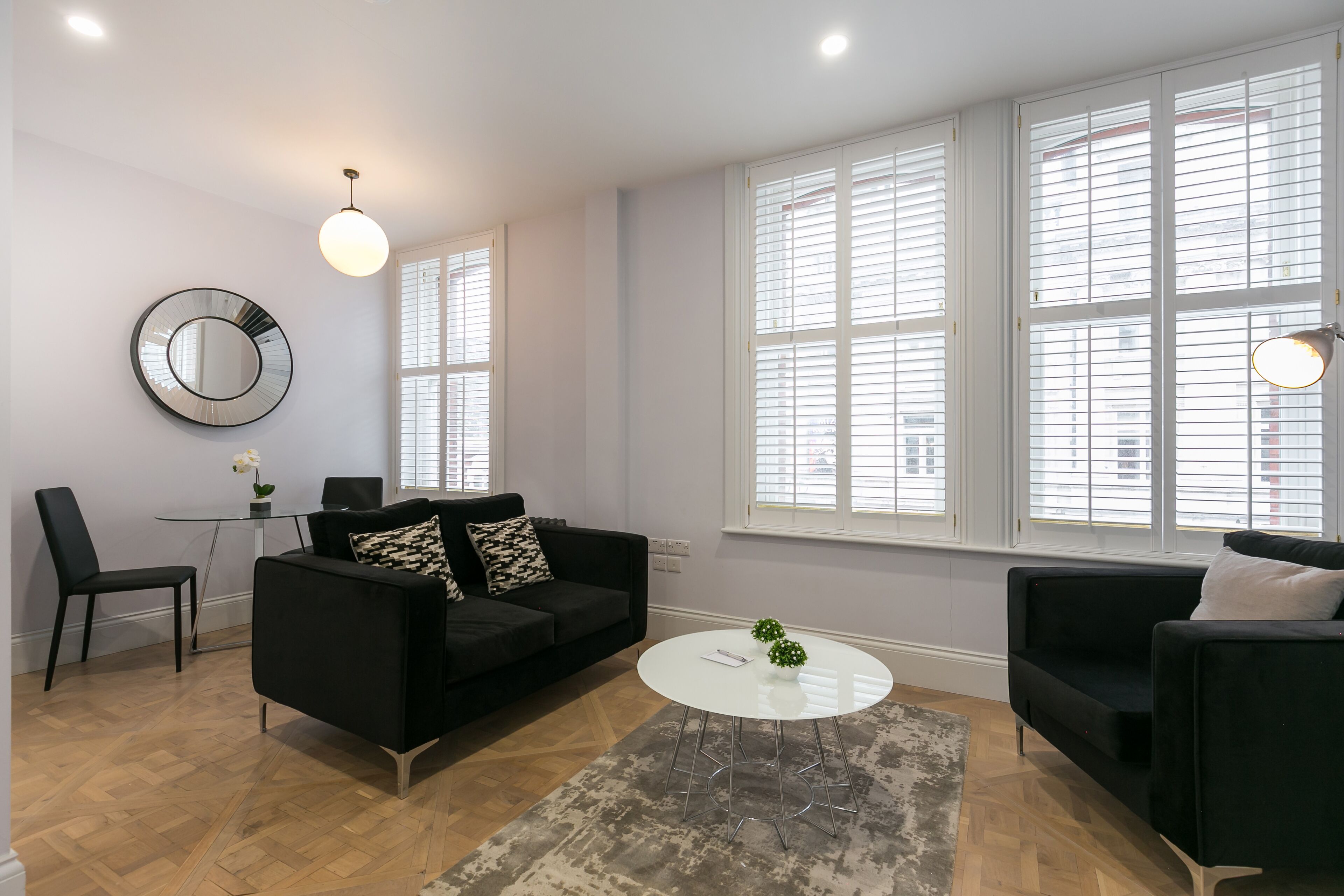 A modern living room with a black sofa, a round coffee table, and a small side table with a flower vase.