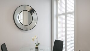 A modern dining area with a glass table, black chairs, a round mirror, and a potted orchid.