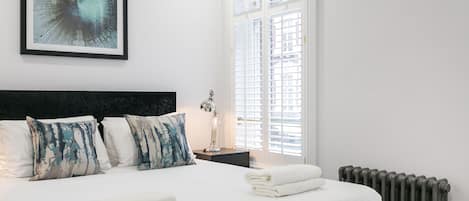 A neatly made bed with white linens and a blue abstract painting above it.